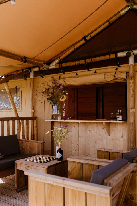 Zona de estar acogedora en una tienda safari, con muebles de madera, ajedrez y flores decorativas.