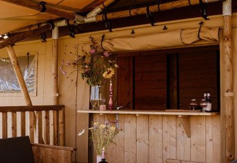 Espace détente d'une tente safari avec mobilier en bois, plateau d’échecs et fleurs décoratives.