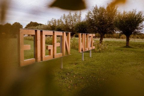 Cartel de madera con las palabras 'EIGEN WIJZE' en el césped del parque vacacional Eigen Wijze en los Países Bajos.
