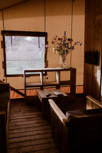 Interieur van een safaritent met houten meubels, gedroogde bloemen in een vaas en zacht licht door het raam.