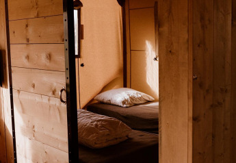 Gemütliches Schlafzimmer im Inneren eines Safarizeltes mit Holzwänden, Bett und warmem Licht.