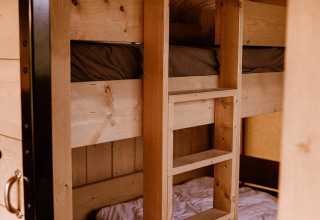 Letti a castello in legno con biancheria bianca e marrone in una tenda safari, visti dall’ingresso.