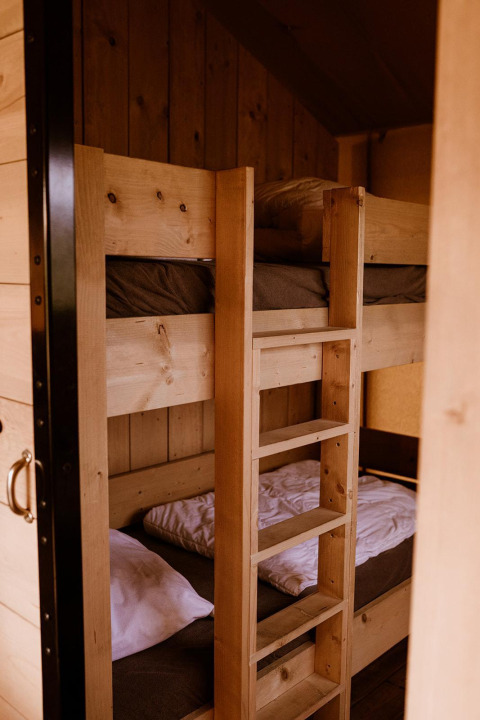 Wooden bunk beds with white and brown bedding inside a safari tent, viewed from an open doorway.