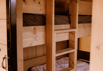 Wooden bunk beds with white and brown bedding inside a safari tent, viewed from an open doorway.