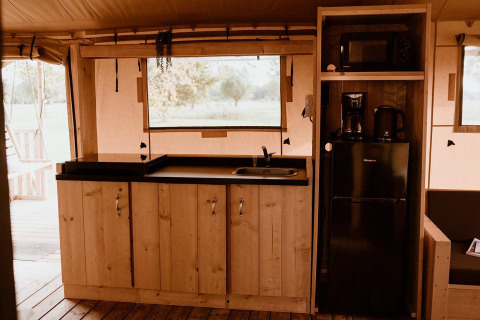 Zona de cocina en una tienda safari con armarios de madera, encimera negra, nevera y cafetera.