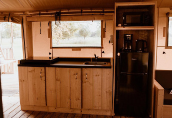 Area cucina in una tenda safari con mobili in legno, piano nero, frigorifero, macchina caffè e microonde.