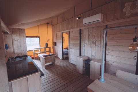 Alojamiento de glamping moderno con suelos y paredes de madera, cocina, comedor y aire acondicionado.