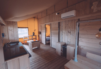 Alloggio glamping moderno con pavimenti e pareti in legno, angolo cucina, zona pranzo e aria condizionata.