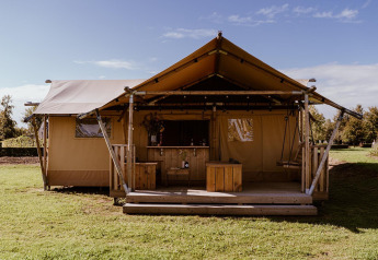 A luxury glamping tent with a wooden deck and swing seat, set in a green open countryside area.