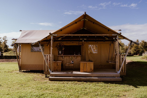 Luxe glamping tent met houten veranda en schommel, gelegen in een groene landelijke omgeving.