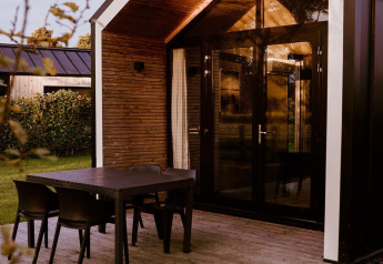 Moderne glamping cabin met grote glazen deuren, houten terras en zwarte tafel met stoelen buiten.