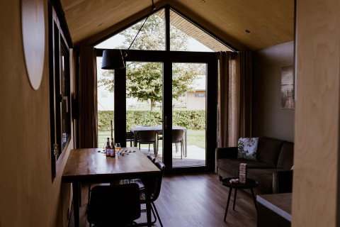 Alojamiento glamping moderno con interior de madera, mesa de comedor, sofá y puertas al jardín.