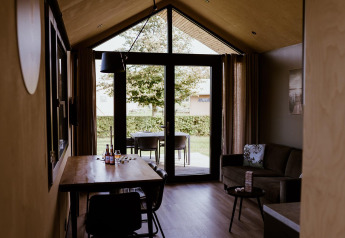 Alloggio glamping moderno con interno in legno, tavolo da pranzo, divano e grandi porte verso il giardino.