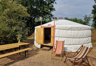 Una yurta mongola con la puerta abierta, sillas de playa y mesa en la naturaleza en Zomerlicht, Países Bajos.