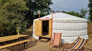 Una yurta mongola con porta aperta, sedie a sdraio e tavolo nella natura a Zomerlicht, Paesi Bassi.