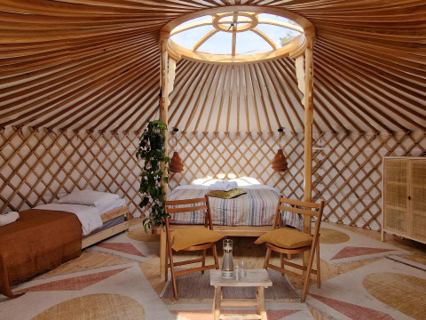 Interior luminoso de una yurta moderna con camas y muebles de madera, en una acogedora casa natural.