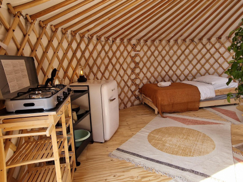 Interior de una casa Nature con cama, cocina pequeña de gas, refrigerador y alfombra decorativa clara.