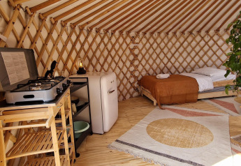 Indretning af et Nature house med seng, lille køkken med gaskomfur, køleskab og dekorative tæpper.