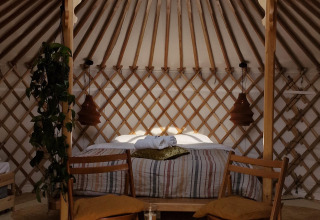 Interno di una casa natura accogliente con sedie in legno, letto, piante e lucernario tipo yurta.