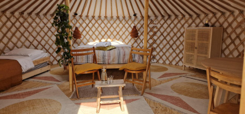 Knusse natuurwoning met tweepersoonsbed, eenpersoonsbed, houten tafels, stoelen en planten in een yurt.
