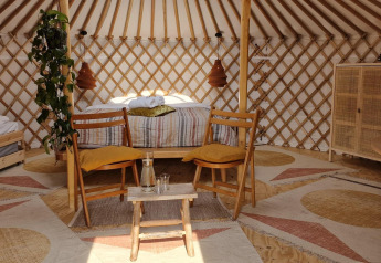 Interno di una casa nella natura con letto matrimoniale, letto singolo, arredo in legno e piante in una yurta.