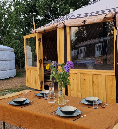 Mesa exterior preparada frente a una Yurt Mongoolse Panorama en Zomerlicht, Países Bajos, rodeada de naturaleza.