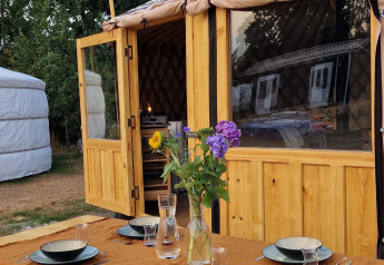 Udendørs spisebord med service foran en Mongoolsk Panorama Yurt ved Zomerlicht i Holland, omgivet af natur.