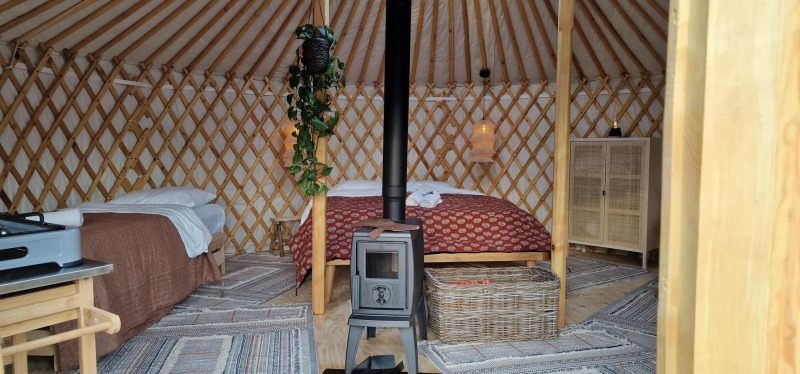 Interior of the Mongoolse Panorama Yurt at Zomerlicht in the Netherlands, with beds, stove, and cozy decor.