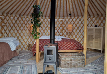 Intérieur de la yourte Mongoolse Panorama à Zomerlicht, Pays-Bas, avec lits, poêle et ambiance chaleureuse.