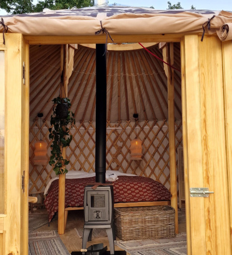 Ingang van een gezellige Mongoolse yurt met houtkachel en bed bij Zomerlicht in Nederland.