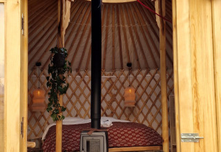 Ingang van een gezellige Mongoolse yurt met houtkachel en bed bij Zomerlicht in Nederland.