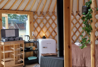 Interior acogedor de una yurta con cocina pequeña, estufa de leña, frigorífico y plantas en Zomerlicht, Países Bajos.