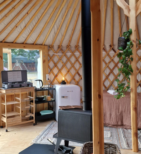 Gemütliches Yurt-Interieur mit kleiner Küche, Holzofen, Mini-Kühlschrank und Pflanzen im Zomerlicht, Niederlande.