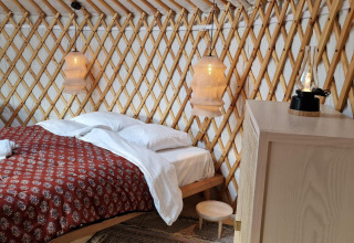 Interior acogedor de la Mongoolse Panorama Yurt en Zomerlicht, Países Bajos, con cama y lámparas cálidas.