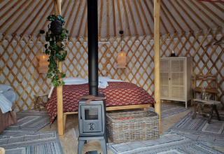 Cozy interior of a Mongolian yurt at Zomerlicht, Netherlands, with beds, wood stove, and rustic decor.