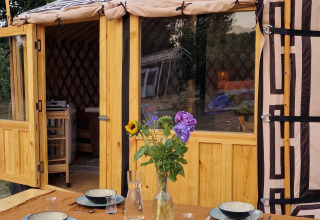 Mesa exterior preparada con platos y flores frente a una yurta mongola en Zomerlicht, Países Bajos.