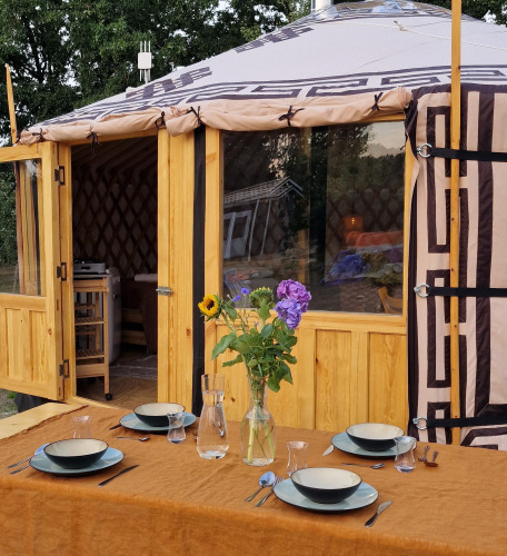Outdoor table set with plates and flowers in front of a Mongolian yurt at Zomerlicht Nature House, Netherlands.