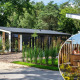 Foto af en moderne lodge omgivet af natur med et indrammet billede af gæster, der slapper af i en udendørs spa.