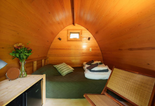 Interior de madera en Duo pød de RØSTIG Dorst, Países Bajos, con cama, silla, ventana pequeña y flores.