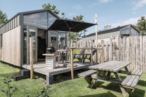 Außenansicht des Rescue cottage bei Duynpark Het Zwanenwater mit Terrasse, Sonnenschirm und Picknicktisch.