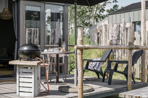 Outdoor terrace at Rescue cottage in Duynpark Het Zwanenwater, Netherlands, with grill, chairs and table.