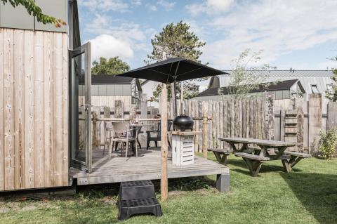 Terrazza esterna con barbecue, ombrellone e tavolo da picnic al Rescue cottage, Duynpark Het Zwanenwater, Paesi Bassi.