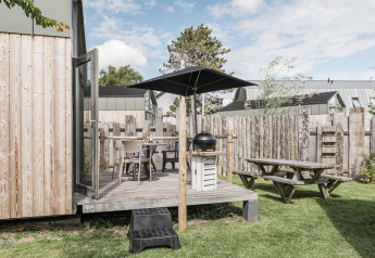 Terrazza esterna con barbecue, ombrellone e tavolo da picnic al Rescue cottage, Duynpark Het Zwanenwater, Paesi Bassi.