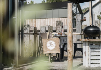 Outdoor deck at Rescue cottage, Duynpark Het Zwanenwater, Netherlands, featuring a grill, chairs, and tote bag.