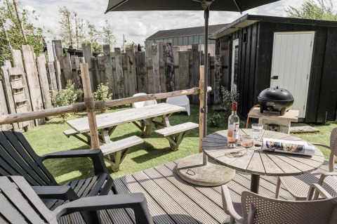Cozy garden setting with picnic bench, grill, wine bottle and chairs at Rescue cottage, Duynpark Het Zwanenwater, Netherlands.