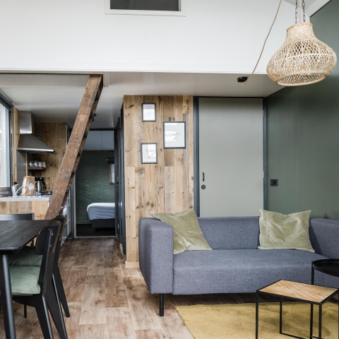 Modern living room inside Rescue cottage at Duynpark Het Zwanenwater, Netherlands, with grey sofa and wood features.