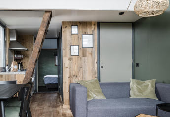 Salón moderno en Rescue cottage, Duynpark Het Zwanenwater, Países Bajos, con sofá gris y detalles en madera.