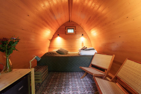 Vista interior del Duo Pod Large en RØSTIG Dorst, Países Bajos, con paredes de madera, cama y sillas.