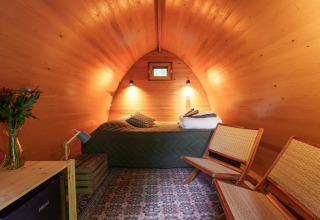 Vista interior del Duo Pod Large en RØSTIG Dorst, Países Bajos, con paredes de madera, cama y sillas.