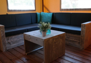 Indoor lounge area in Luxury Lodge Safari Tent with wooden furniture and black cushions at De Kleine Belties.